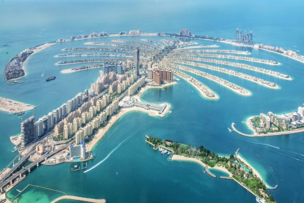 Aerial view of Palm Jumeirah in Dubai, a man-made island shaped like a palm tree, featuring rows of luxurious buildings, villas, and clear blue waters surrounding the structure.